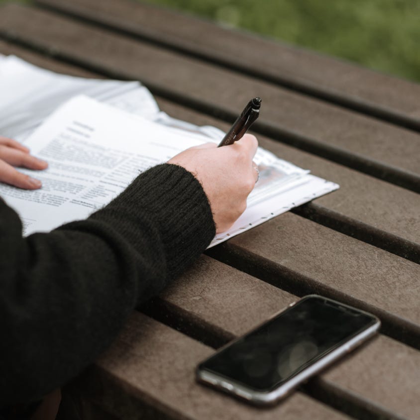 From above of crop anonymous female writing with pen in documents on wooden table in park